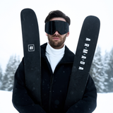 Man wearing Jack magnetic ski goggles, holding skis in the snow
